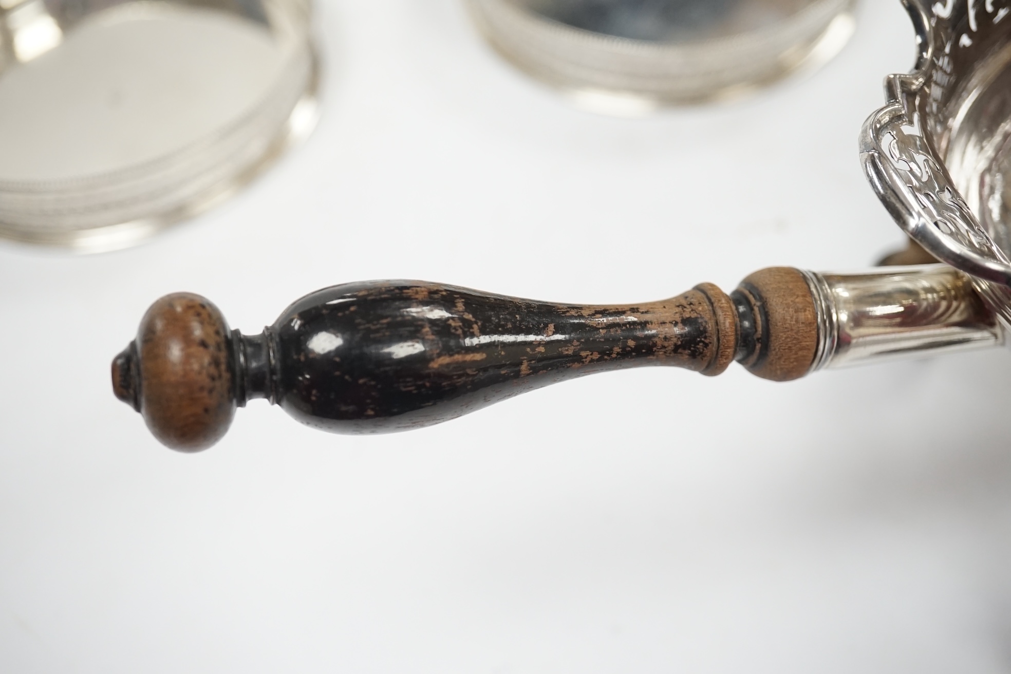 An early 19th century Dutch white metal bowl, with pierced border and turned wooden handle, length 27cm, (a.f.), together with a pair of continental white metal mounted wine coasters, diameter 12.7cm. Condition - poor to